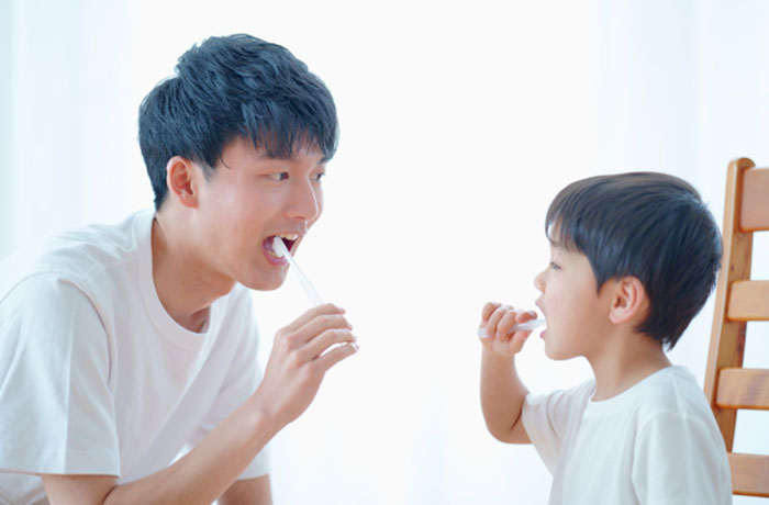 子供の歯磨き習慣を教える父親と楽しそうに磨く男の子のイメージ